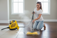 Woman using a vapamore steam cleaner on a wooden floor in a bright room.