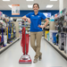 Woman in a blue shirt holding a red Sanitaire vacuum cleaner in a store aisle.