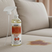Bottle of Stain-X stain and odor remover on a beige couch with a stain.