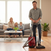 Man holding a Miele C1 Centennial vacuum cleaner in a living room with a family sitting on the couch. Capital Vacuum Raleigh Cary NC