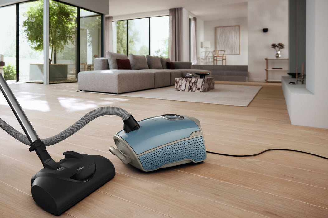 Miele Guard L1  Nordic Blue vacuum cleaner on a wooden floor with a modern living room in the background