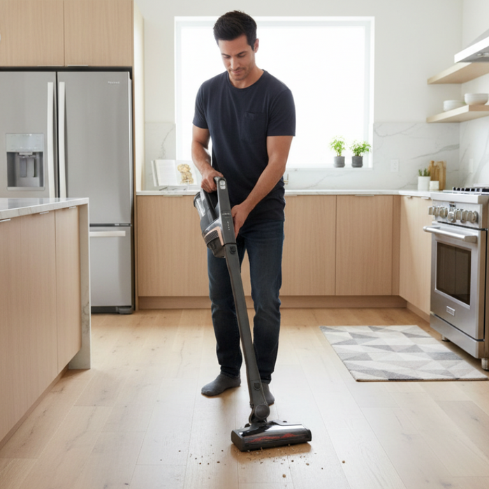 Man using a cordless vacuum cleaner in a modern kitchen.