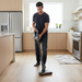 Man using a cordless vacuum cleaner in a modern kitchen.