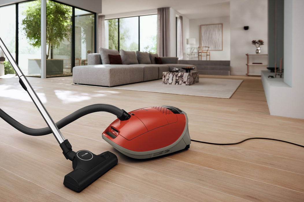 Red Miele vacuum cleaner on a wooden floor in a modern living room. Miele Guard M1 Terra Red SVWE0 Canister Vacuum Cleaner Capital Vacuum Raleigh Cary NC