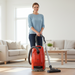 Woman using a red Miele vacuum cleaner in a living room. Miele Guard M1 Terra Red SVWE0 Canister Vacuum Cleaner Capital Vacuum Raleigh Cary NC
