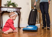 Child watching a woman using a Riccar R10CV vacuum cleaner on a wooden floor. Capital Vacuum Raleigh Cary NC