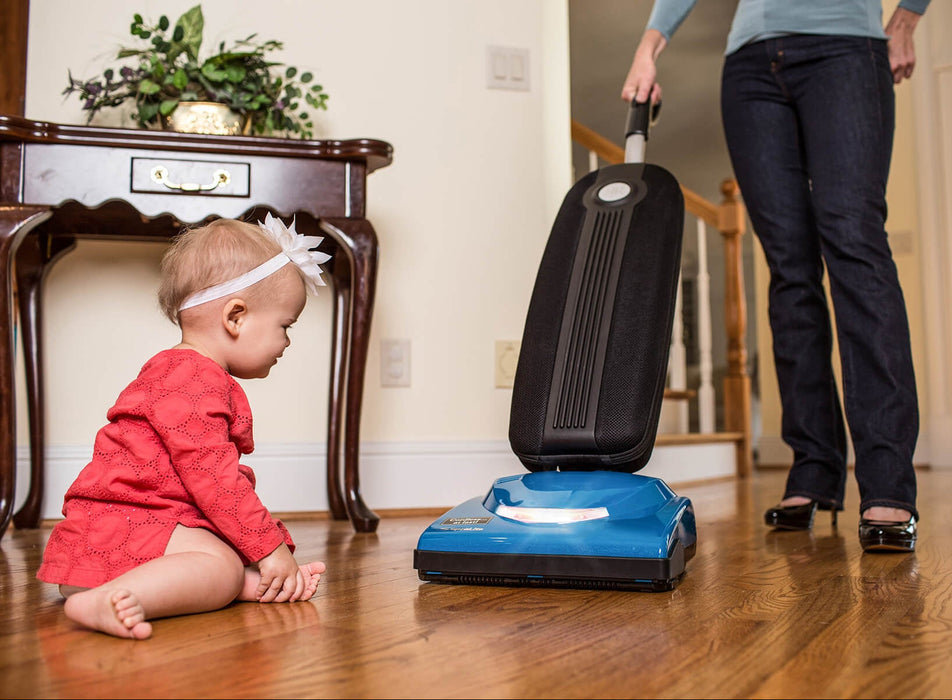 Child watching a woman using a Riccar R10CV vacuum cleaner on a wooden floor. Capital Vacuum Raleigh Cary NC