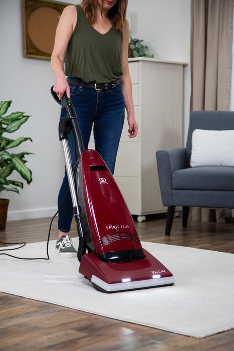 Woman using a Riccar R21 Spirit Plus red vacuum cleaner on a wooden floor in a living room. Riccar R21 Spirit Plus Upright Vacuum Capital Vacuum Raleigh Cary NC