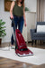 Woman using a Riccar R21 Spirit Plus red vacuum cleaner on a wooden floor in a living room. Riccar R21 Spirit Plus Upright Vacuum Capital Vacuum Raleigh Cary NC