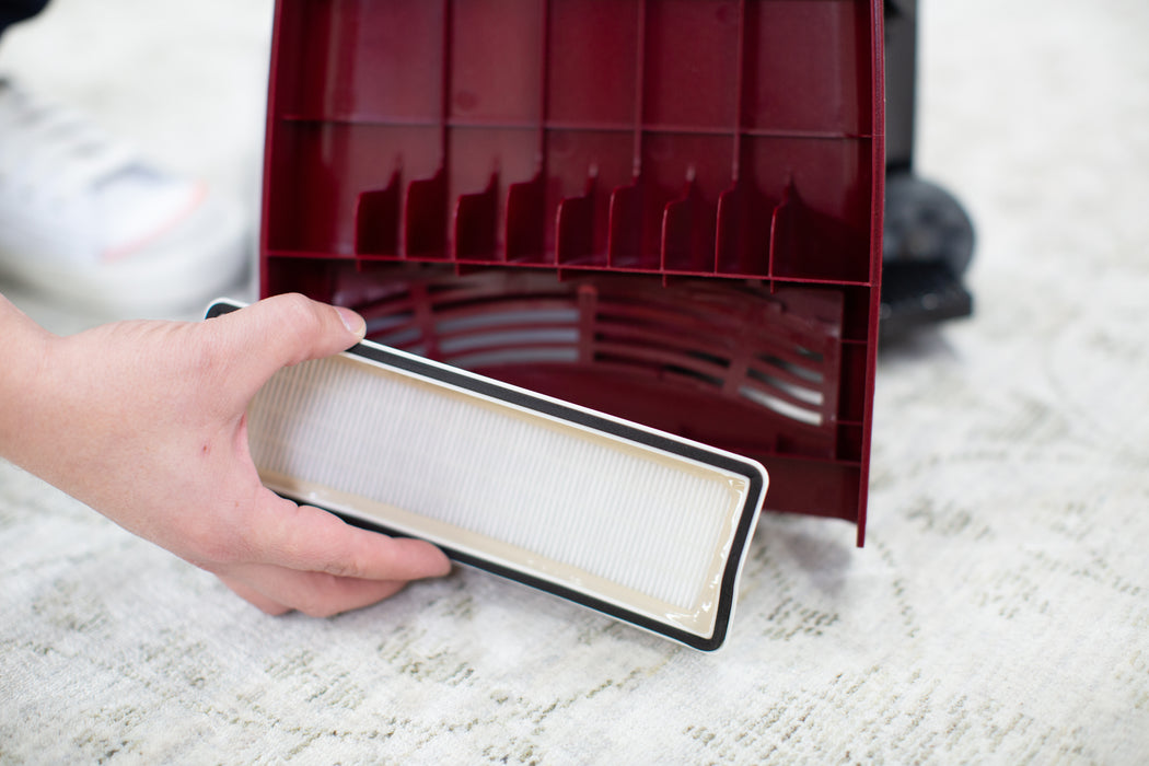 Person holding a HEPA filter in front of a red Riccar R21 Spirit Plus on a light-colored carpet. Riccar R21 Spirit Plus Upright Vacuum Capital Vacuum Raleigh Cary NC