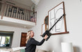 Person using a Riccar R65 cordless vacuum cleaner to clean a wall-mounted picture frame in a living room. Capital Vacuum Raleigh Cary NC