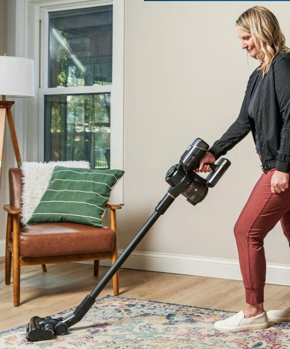 Woman using a Riccar R65 cordless vacuum cleaner in a living room. Capital Vacuum Raleigh Cary NC