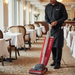 Person cleaning a restaurant floor with a red Sanitaire vacuum cleaner.