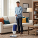 Man cleaning a carpet with a Sebo vacuum cleaner in a living room.